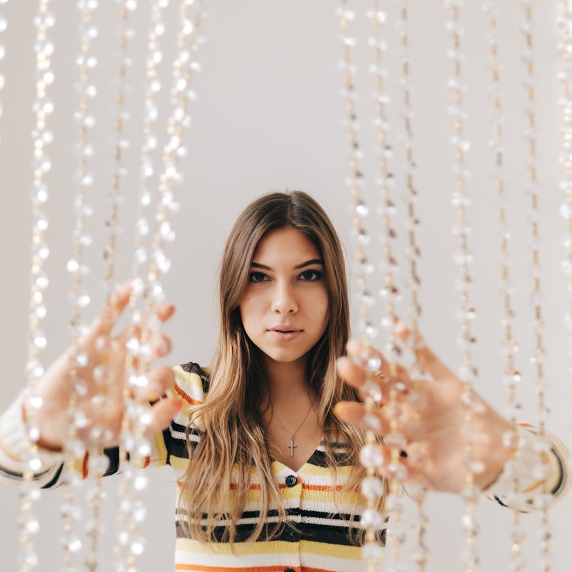 Young woman parting a beaded curtain, embracing the April 11, 2022 weekly horoscope for her zodiac s...