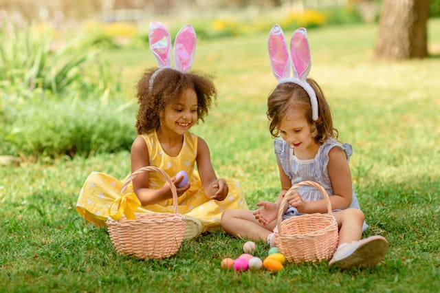 Two children wearing Bunny ears find and pick up multicolored egg on Easter egg hunt in garden