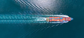 Aerial top view of cargo maritime ship with contrail in the ocean ship carrying container and runnin...