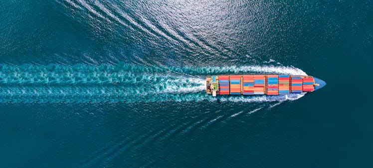 Aerial top view of cargo maritime ship with contrail in the ocean ship carrying container 