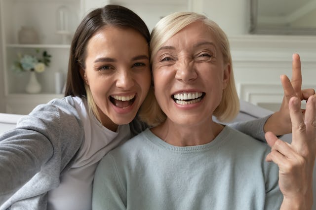 Smiling millennial girl child take selfie with overjoyed funny elderly mother at home, happy grown-u...