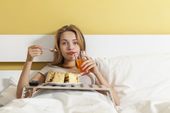 Teen girl drinking soda, eating cake in bed and watching TV