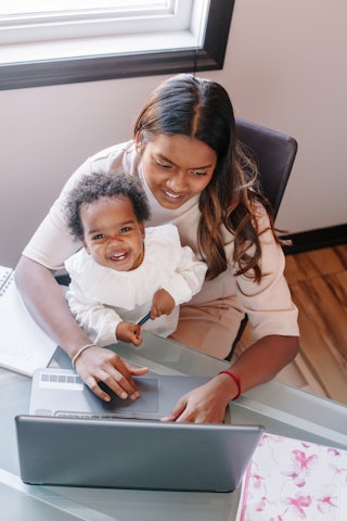 Mixed race Indian mother with African black baby working online from home on Internet. Workplace of ...