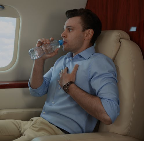 Nervous young man with aviophobia drinking water in airplane