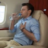 Nervous young man with aviophobia drinking water in airplane