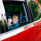 Adorable toddler girl sitting in car seat, holding plush soft toy and looking out of the window on n...