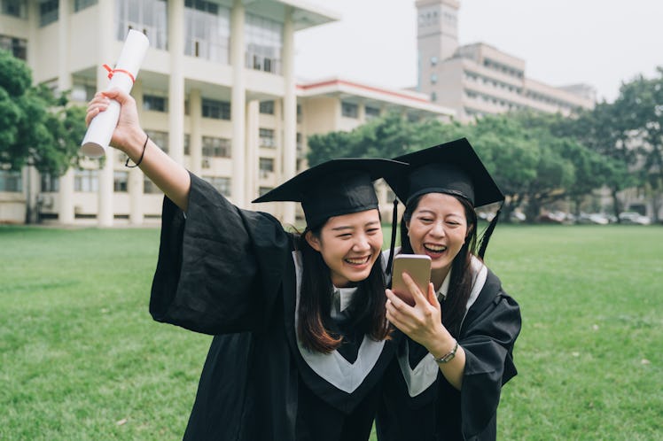 Two graduates laugh reading grad puns they'll be using for funny graduation Instagram captions.