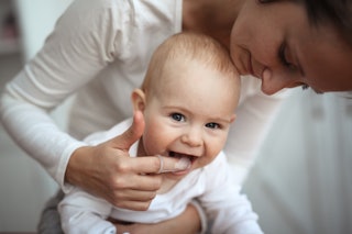 Mom helps to brush the teeth of a happy baby, Hygiene of the baby’s mouth, brushes her teeth with a ...