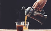 Coffee is poured into a cup from French press coffee maker , On the  old wood table and black backgr...