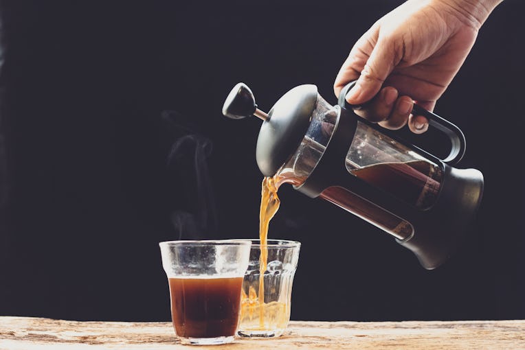 Coffee is poured into a cup from French press coffee maker , On the old wood table and black backgr...