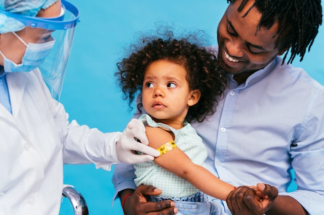 A healthcare worker applies a band-aid to the arm of a young child sitting in a parent's lap. Childr...