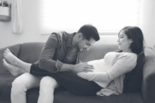 Man holding pregnant woman's belly while they're on the couch