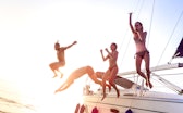 Young millenial friends jumping from sailboat at sea ocean trip - Guys and girls having summer fun t...
