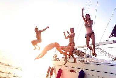 Young millenial friends jumping from sailboat at sea ocean trip - Guys and girls having summer fun t...