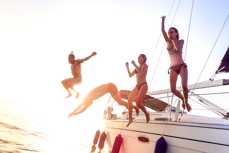 Young millenial friends jumping from sailboat at sea ocean trip - Guys and girls having summer fun t...