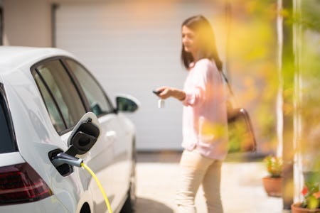 Close up of a electric car charger with female silhouette in the background, locking a car