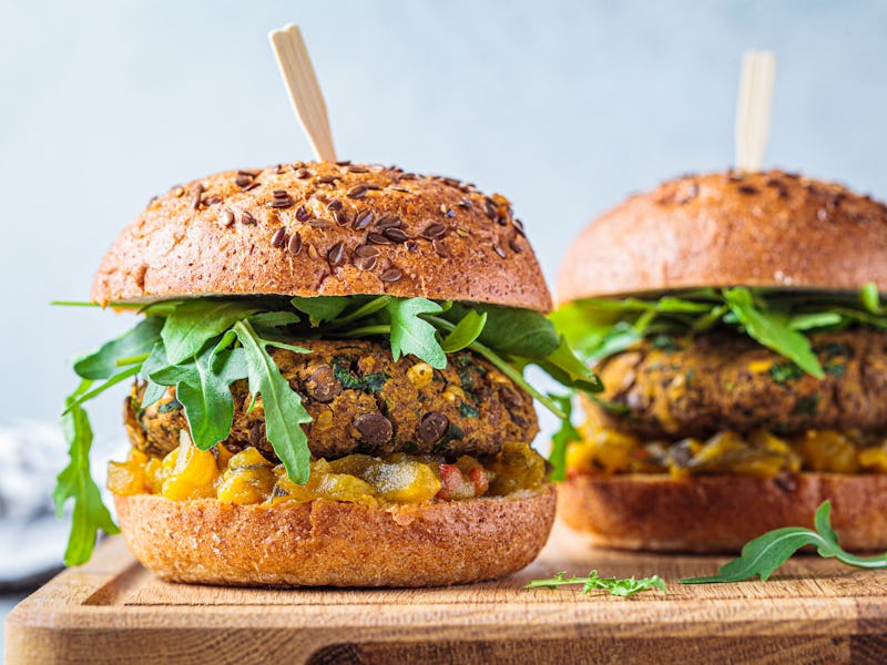 Vegan lentil burger with arugula, mustard sauce, fresh vegetables and sweet potato fries on a wooden...