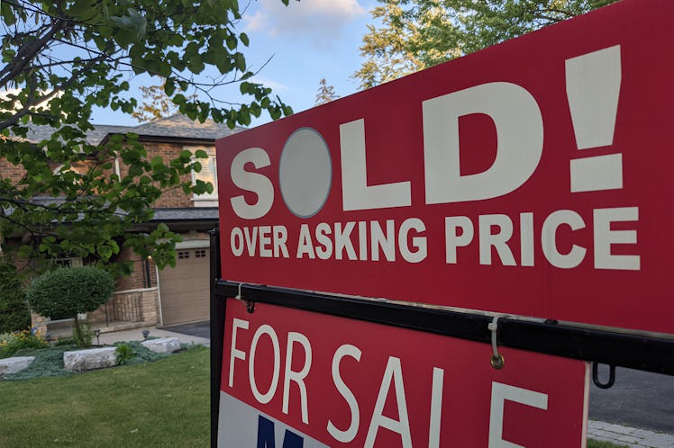 New "sold" sign over asking price for sale in front of house in residential area.