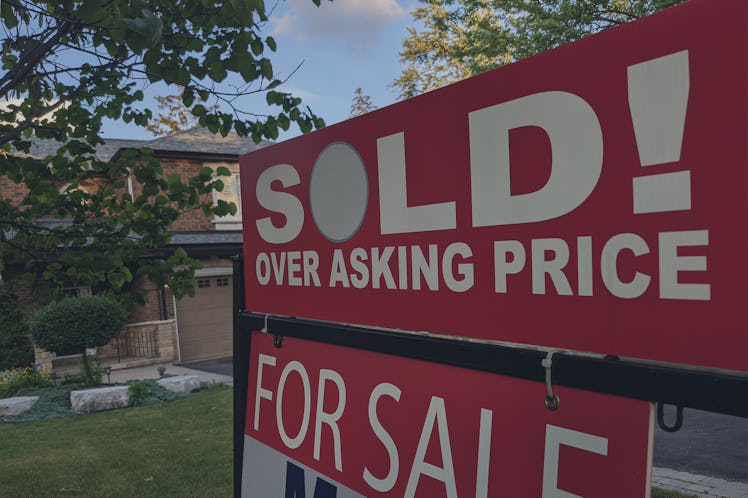 New "sold" sign over asking price for sale in front of house in residential area.