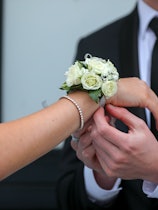 A corsage being placed on a teenagers wrist for a prom date.   