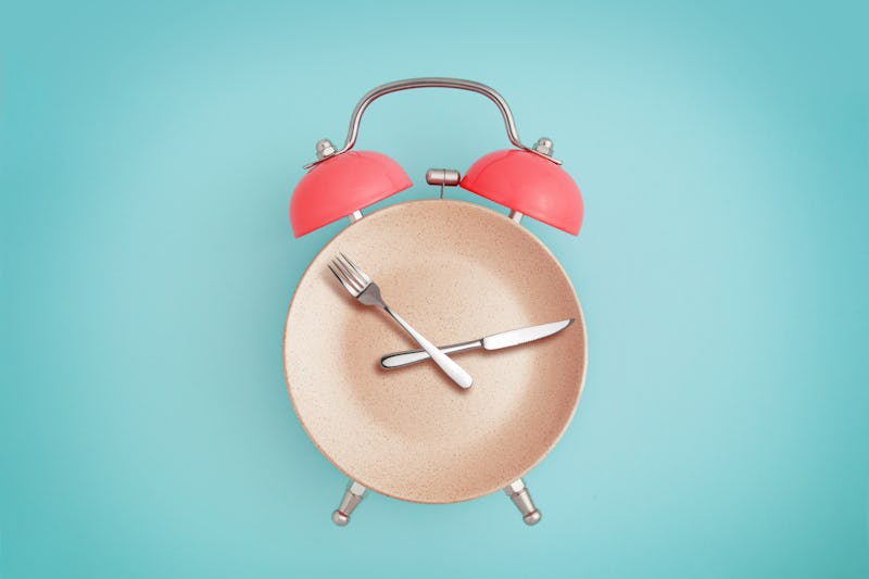 Alarm clock and plate with cutlery . Concept of intermittent fasting, lunchtime, diet and weight los...