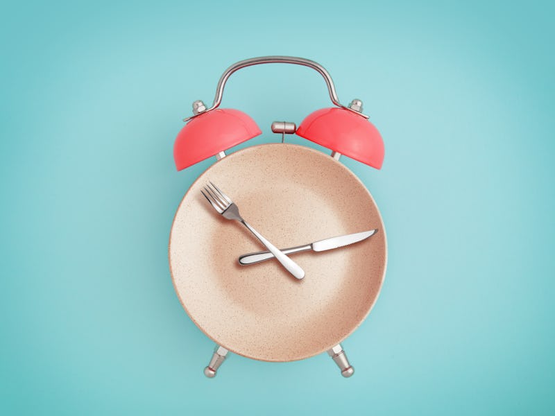 Alarm clock and plate with cutlery . Concept of intermittent fasting, lunchtime, diet and weight los...