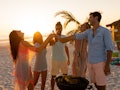 A multi-ethnic group of friends enjoying their time together on a beach during sunset, drinking beer...