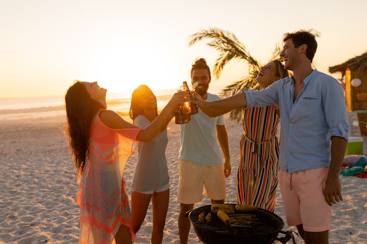 A multi-ethnic group of friends enjoying their time together on a beach during sunset, drinking beer...