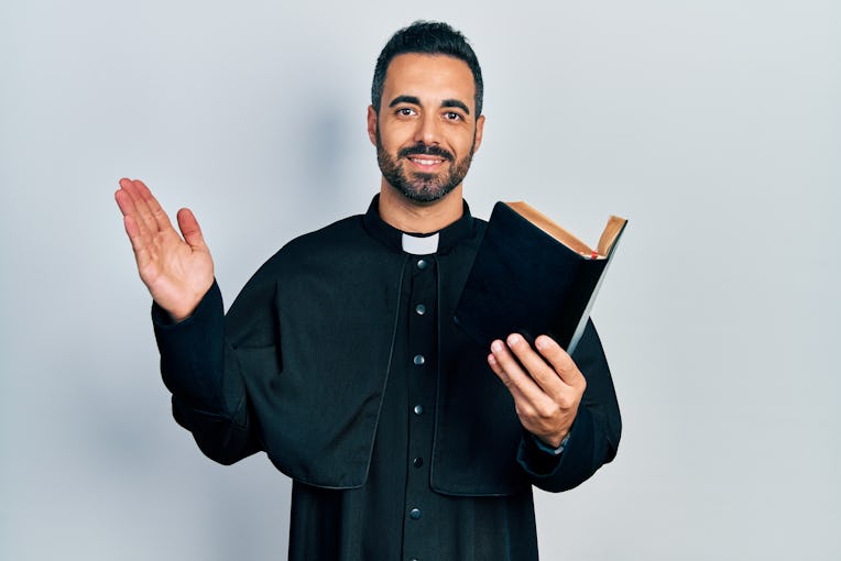 Handsome hispanic priest man with beard holding bible and christian cross smiling with a happy and c...