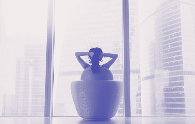 Young model sitting in armchair, hands crossed behind head, looking through panoramic glass wall at ...