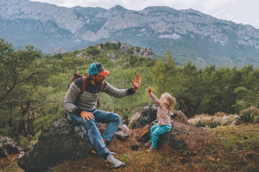 A dad and his daughter high five while on a hike in a beautiful wooded area