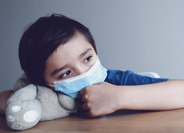 A child in a face mask rests his head on a table, showing fatigue, a common symptom of long COVID in...