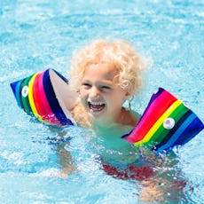 Child in swimming pool wearing colorful inflatable armbands. Kids learn to swim with float aid. Floa...