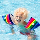 Child in swimming pool wearing colorful inflatable armbands. Kids learn to swim with float aid. Floa...