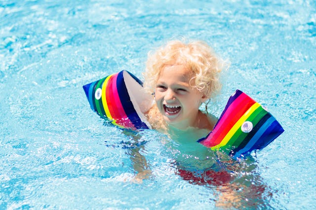 Child in swimming pool wearing colorful inflatable armbands. Kids learn to swim with float aid. Floa...