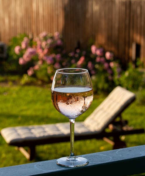 Rosé in a wine glass on the porch with a comfortable deck chair and blooming rose bushes in the back...