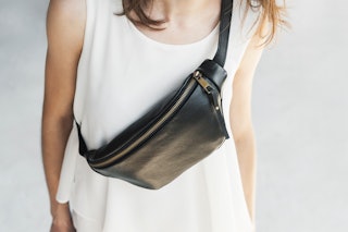 Leather sling bag, Fanny pack woman. Girl in a white T-shirt wears a black banana bag, close-up.