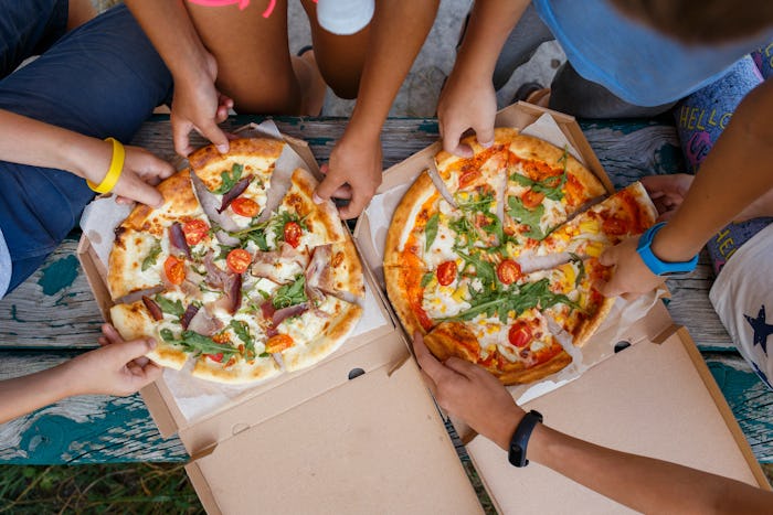Top view image of children grab slices of pizza from box at the outdoors picnic. Children hands taki...