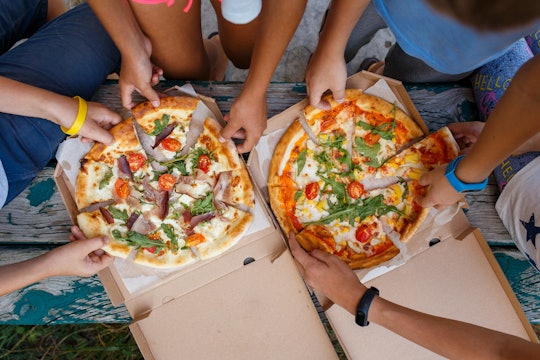 Top view image of children grab slices of pizza from box at the outdoors picnic. Children hands taki...