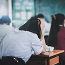 A student leans her head against her hand in a classroom; tired