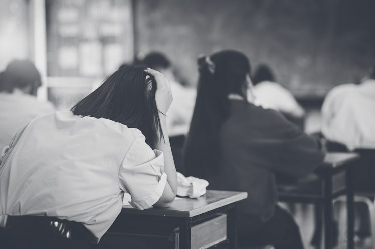 A student leans her head against her hand in a classroom; tired