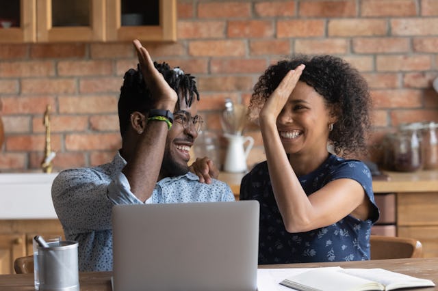 Happy excited Black mixed race couple celebrating financial success at laptop, getting income, loan,...
