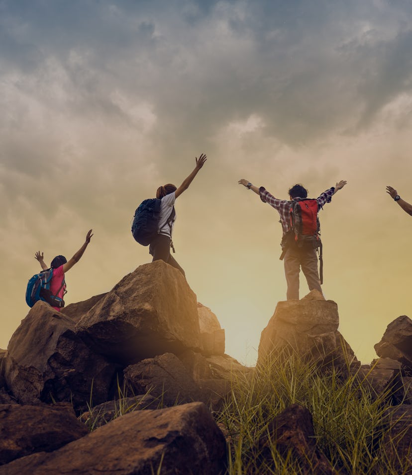 Adventure to overcome the limits of life, male and female hikers climbing up mountain cliff under su...