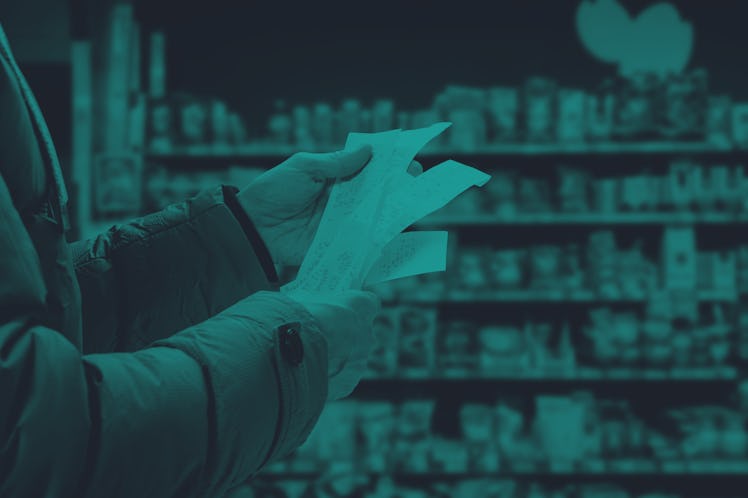 A person in a brown puffy coat looks at their receipts in the supermarket with a shelf of goods out ...