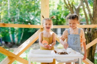 Happy sister kids play with sand and water in sensory baskets on the outdoor sensory table, sensory ...