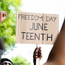A cardboard sign that reads "Freedom Day Juneteenth" with fists raised up