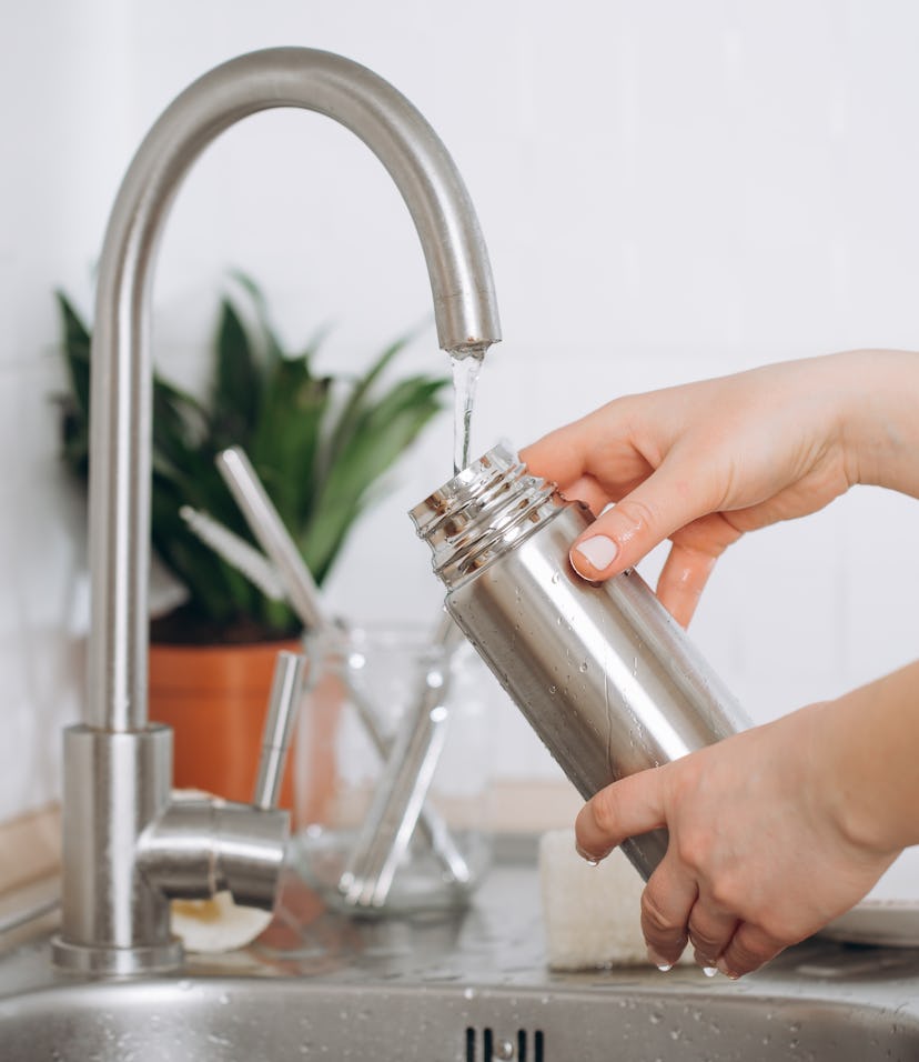 Two hands washing a metal reusable bottle in a sink, demonstrating how to clean a reusable water bot...