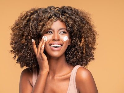 Beautiful afro woman with a cream on face. Skin care concept.