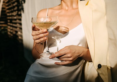 Luxurious woman wearing a white dress, holding a coupe with champagne in sun light. Concept of an op...
