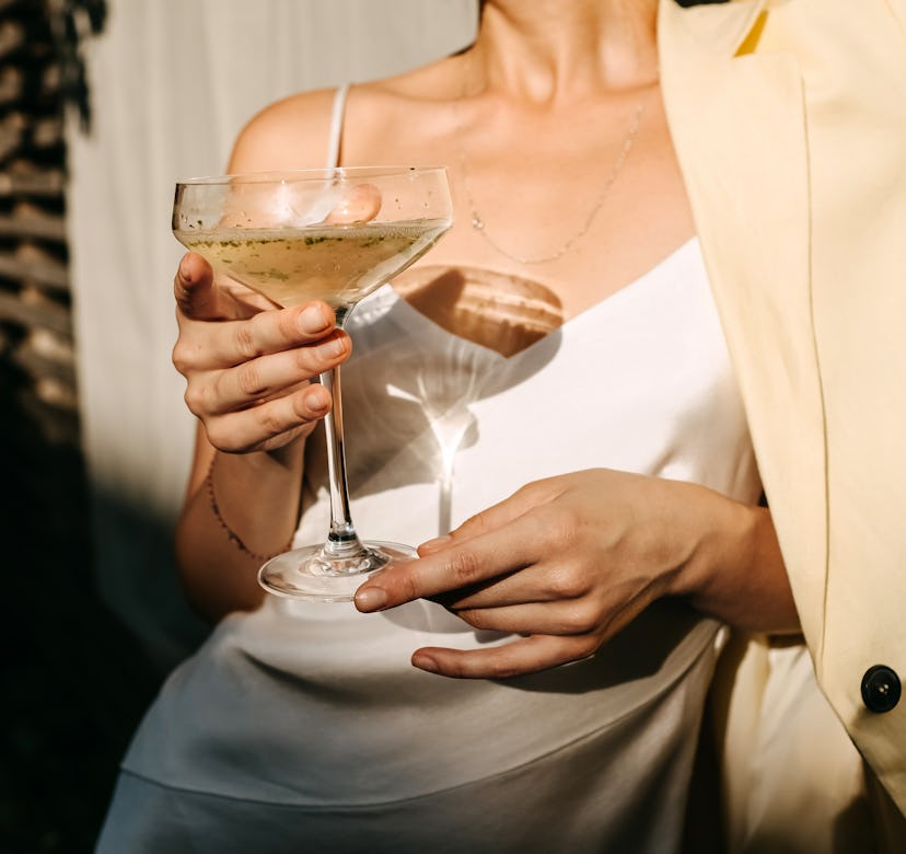 Luxurious woman wearing a white dress, holding a coupe with champagne in sun light. Concept of an op...